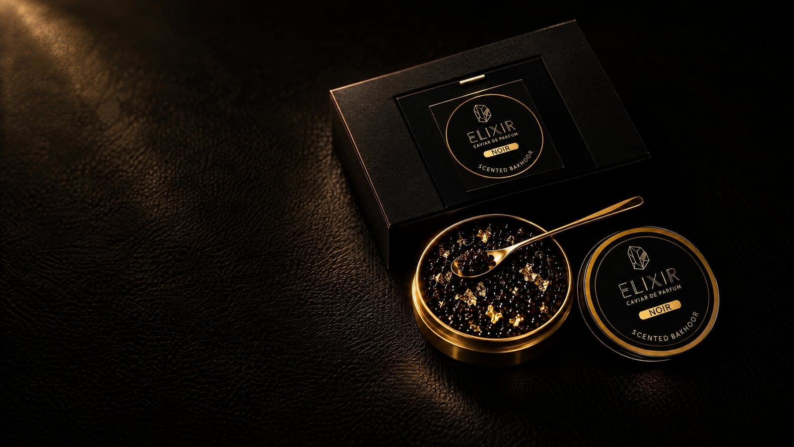 Noir: the open tin of pearls flecked with gold leaf, a gold spoon, the closed tin and its box, on black leather