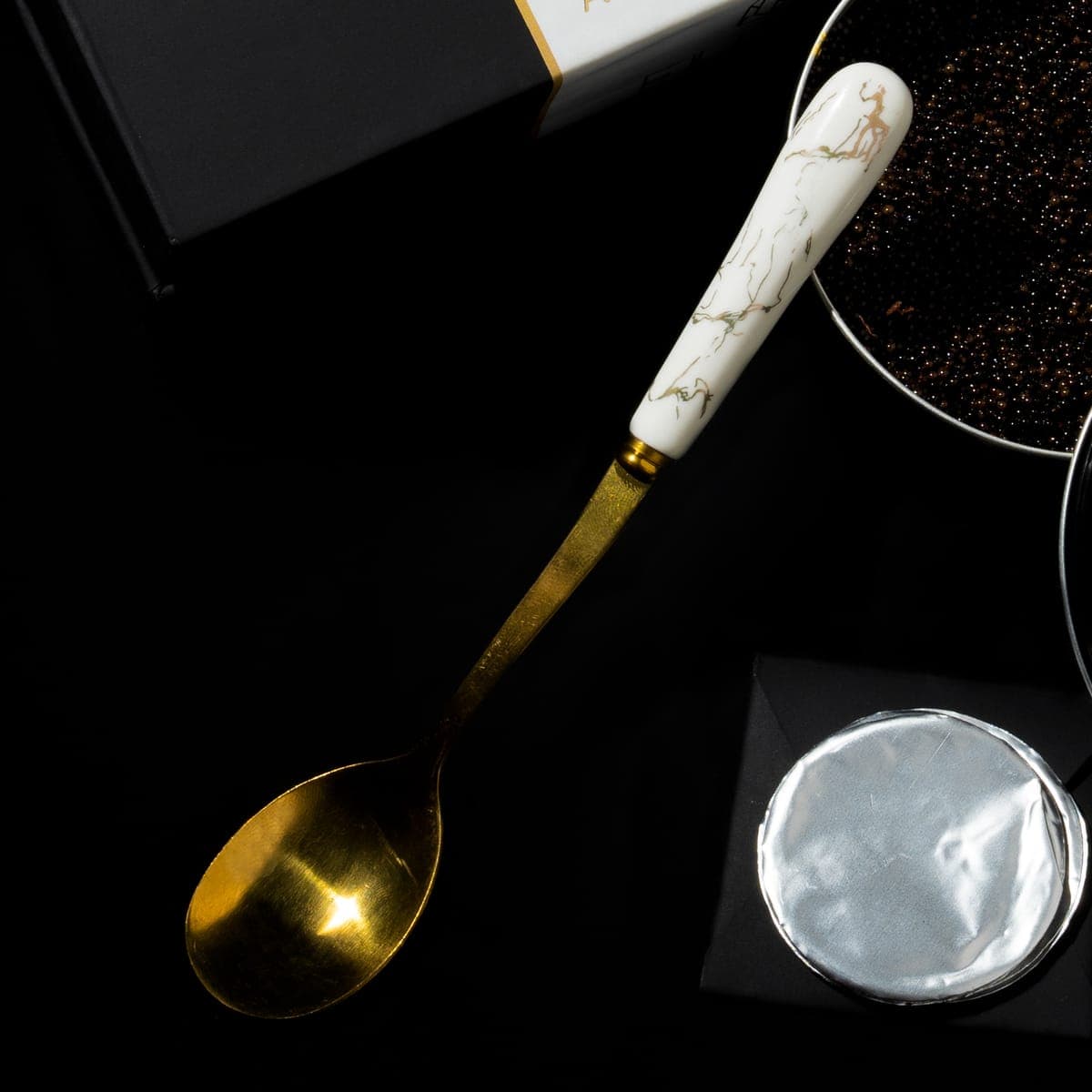 The gold spoon with its marbled handle, beside a disc of foil