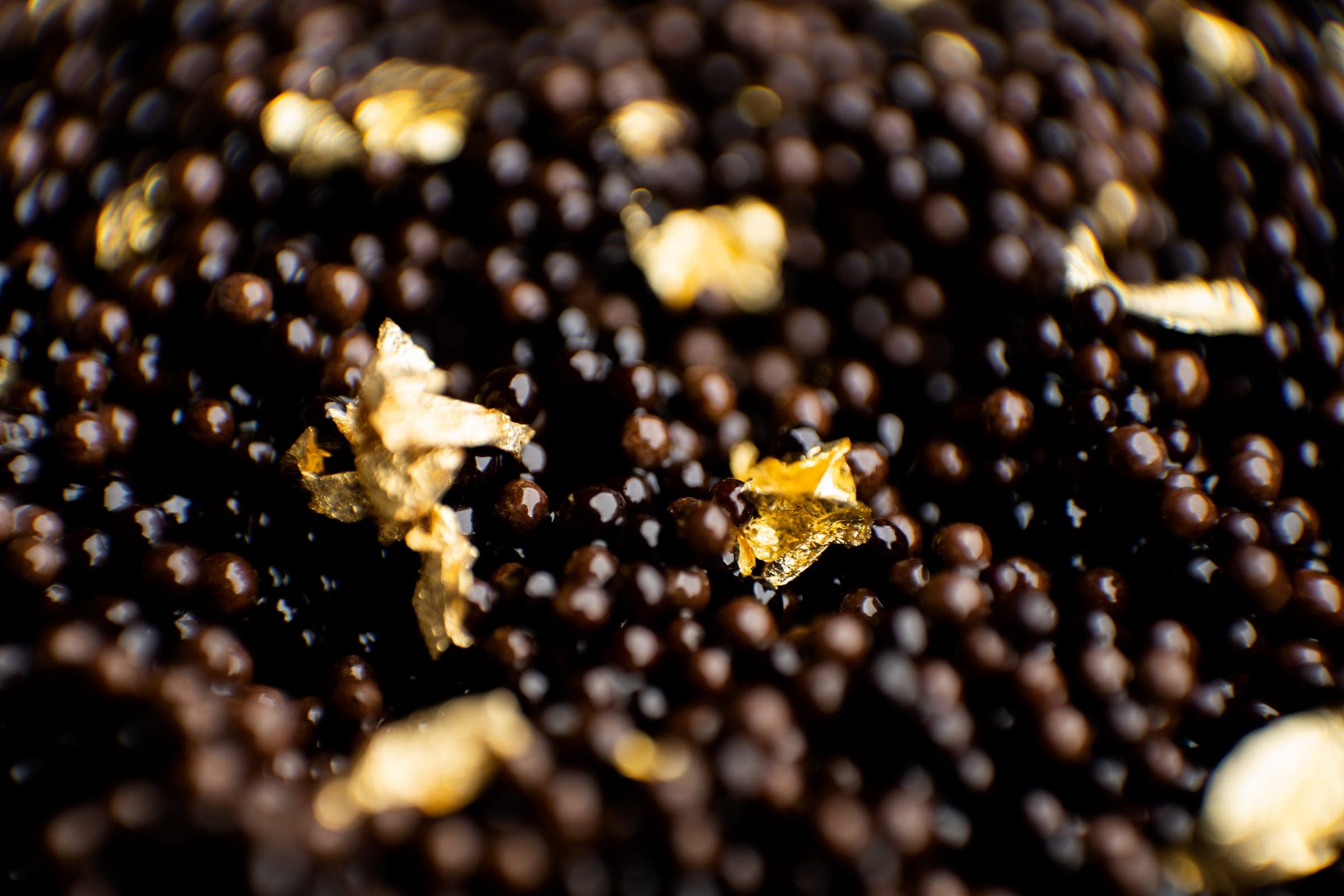 Macro of Caviar Bakhoor pearls, dark spheres scattered with flakes of 24-karat gold leaf
